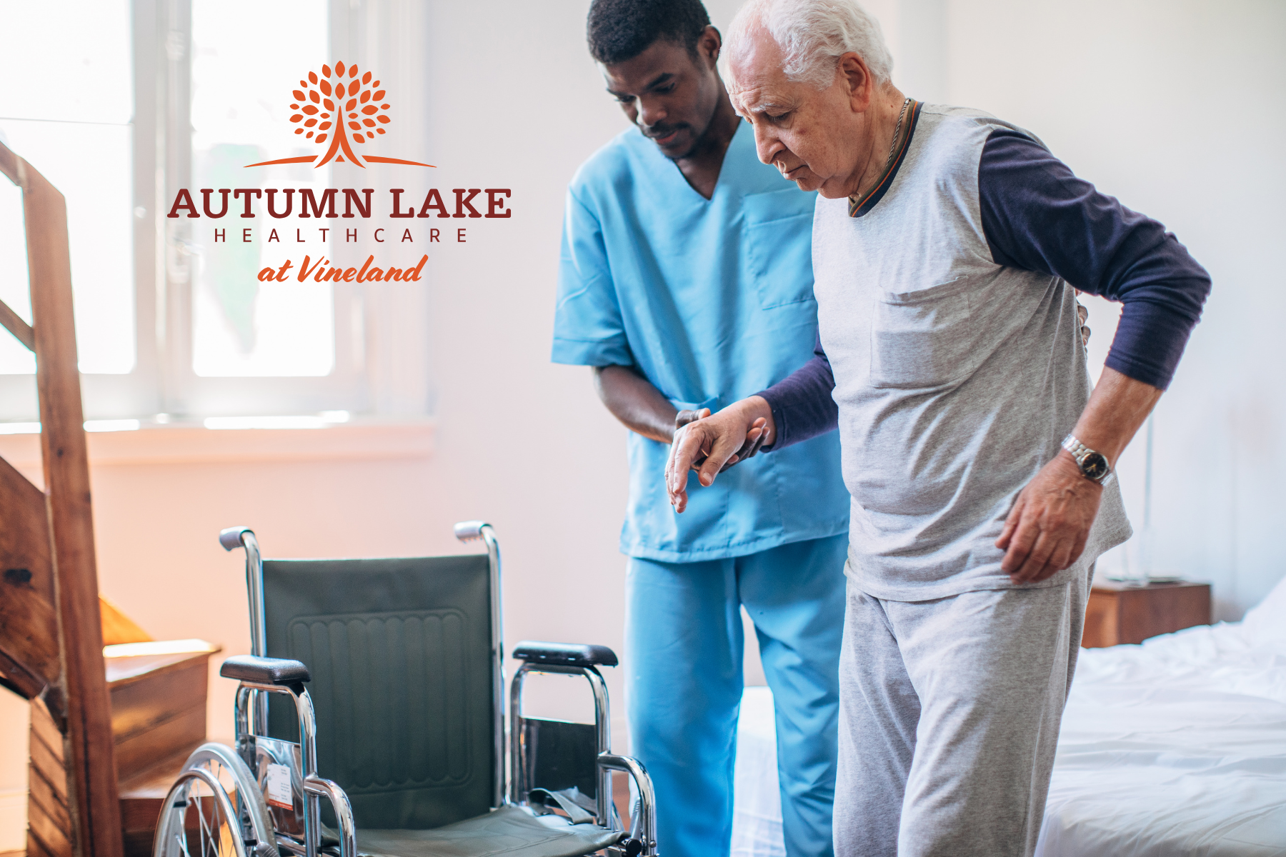 A male nurse in scrubs assists an elderly man with mobility near a wheelchair